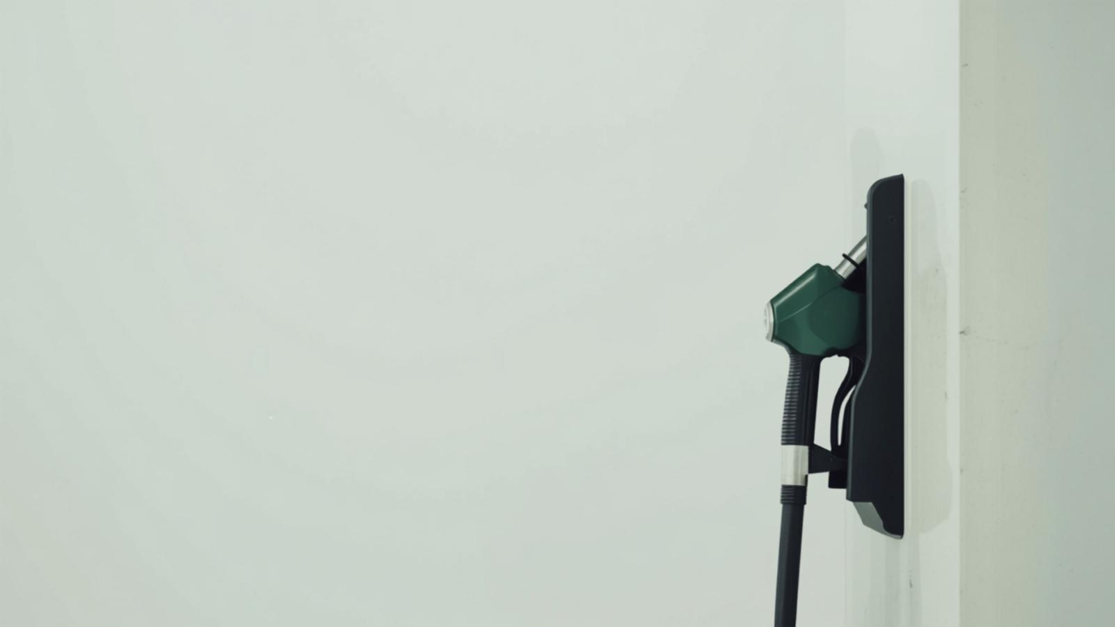 A fuel pump nozzle resting in its holster at a quiet forecourt in daylight
